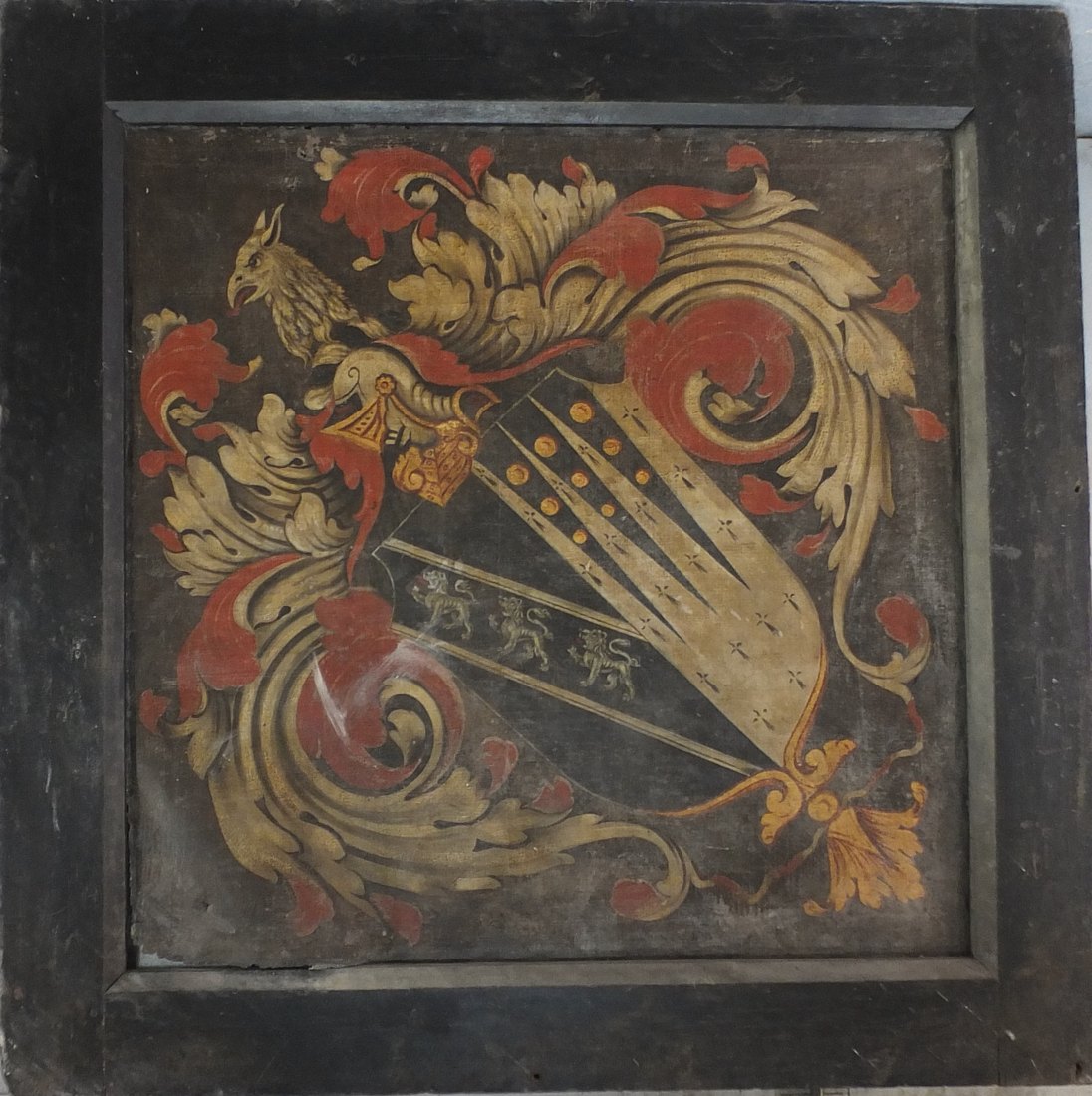 Powerstock hatchment before conservation: a square framed heraldic panel, its griffin crest, scrolling mantling and shield dulled to muted reds and ochres under dirt and discoloured varnish